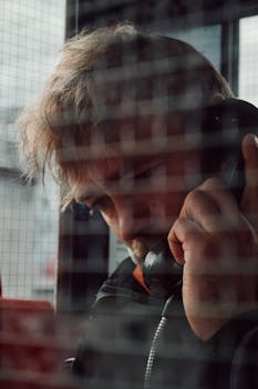 A thoughtful man using a payphone inside a booth in Oslo, creating an introspective mood.