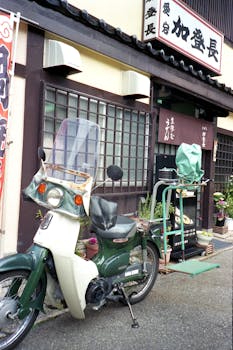 Green motorcycle parked outside a traditional Japanese restaurant facade on a city street.