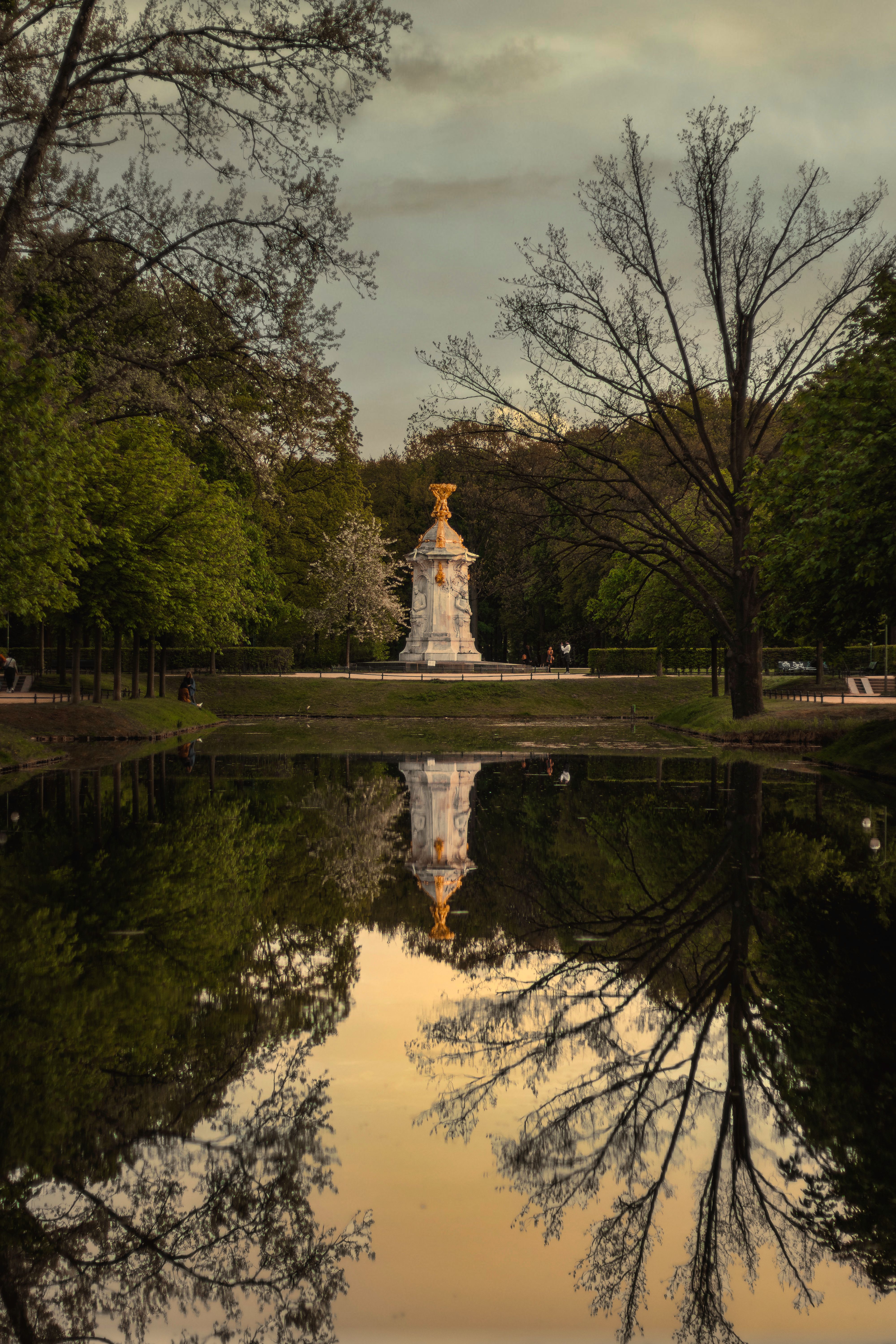 Serene park scene with water reflections of trees and monument at sunset.