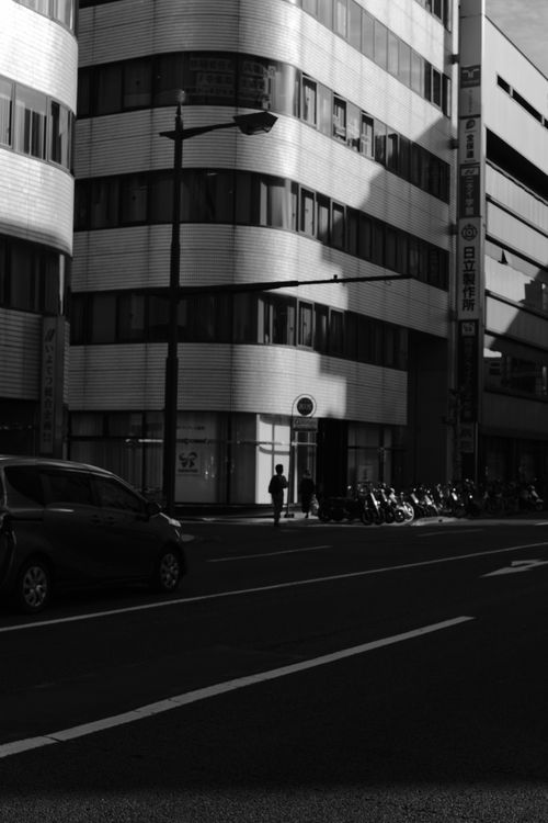 Free Moody black and white urban photograph featuring a street with a moving car and modern buildings. Stock Photo