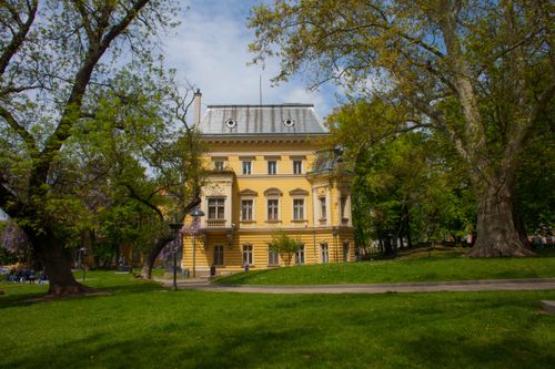 Free Yellow historic building surrounded by lush park and trees under a clear sky. Stock Photo