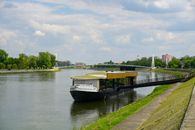 A tranquil scene of the Drava River with a boat and footbridge in Osijek, Croatia, on a sunny day.