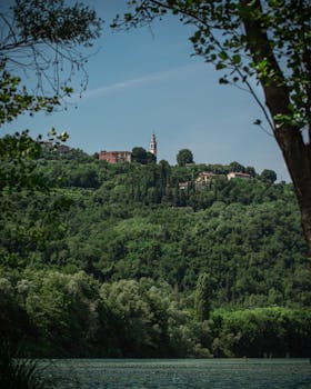 Lush green hills and historic church in Veneto, Italy under clear blue skies.