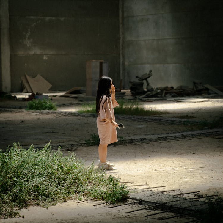 Young Girl Wearing A Beige Big Shirt Standing Alone On A Dark Vacant Lot