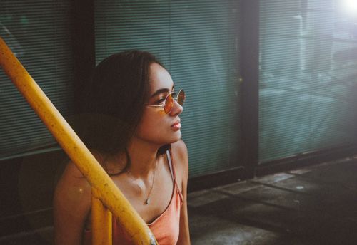 Free Fashionable woman with sunglasses and spaghetti strap top on a city stairway, enjoying sunlight. Stock Photo