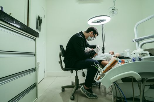A dentist wearing a mask treats a patient in a modern dental clinic in Brazil.