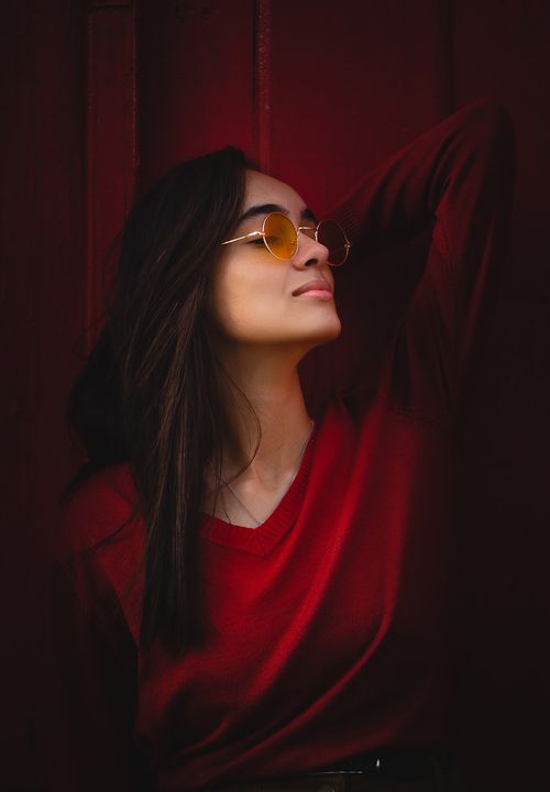Free Young woman in red sweater posing with sunglasses, exuding confidence and style. Stock Photo