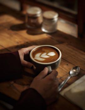 Close-up of hands holding a latte with beautiful art in a cozy setting.