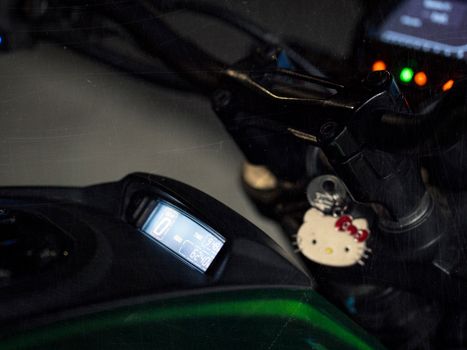 Detailed close-up of a motorcycle dashboard featuring an illuminated display and a Hello Kitty keychain.