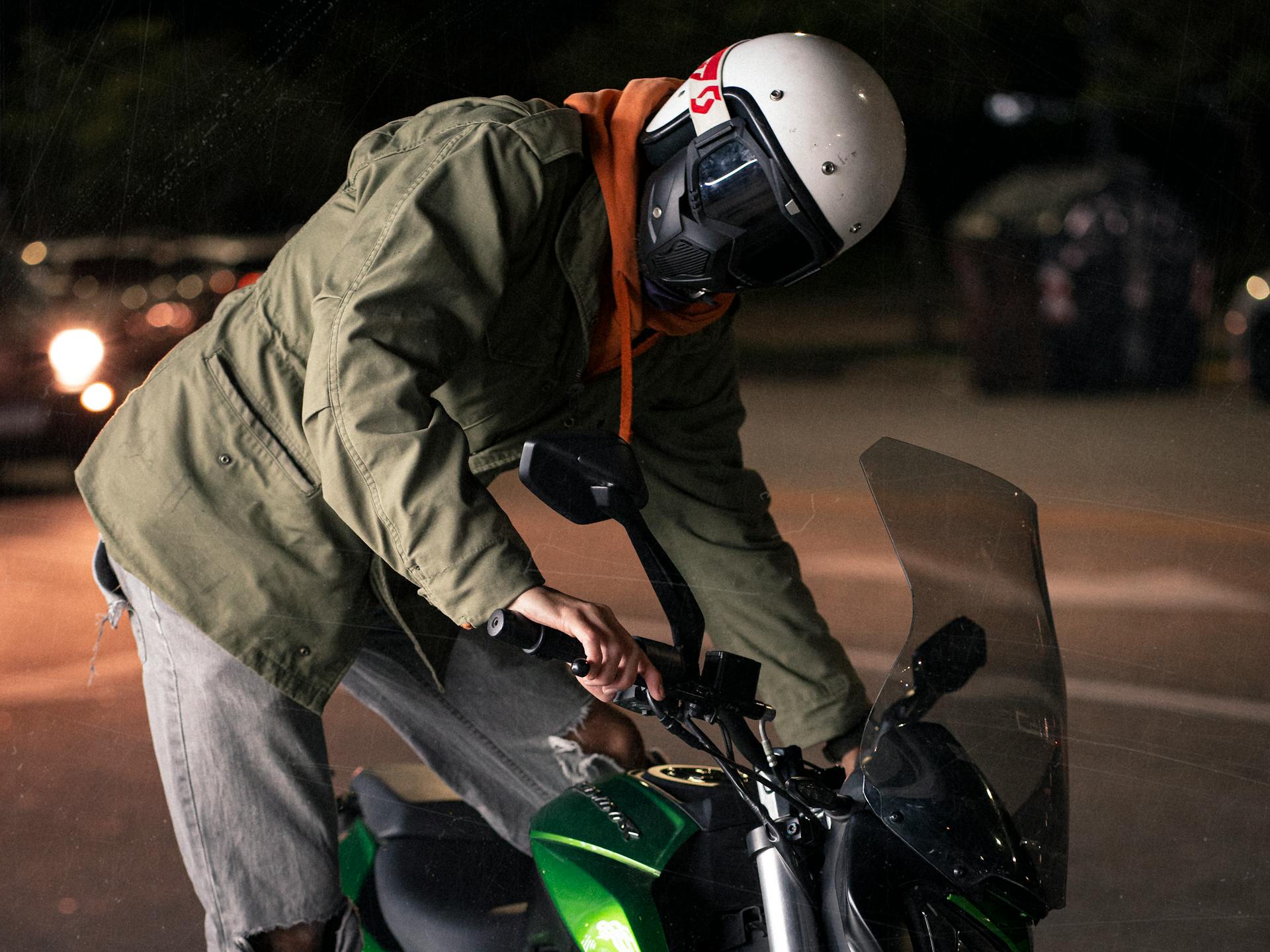 Motorcyclist in helmet and jacket posing on a green sports bike at night, capturing urban adventure and safety gear.