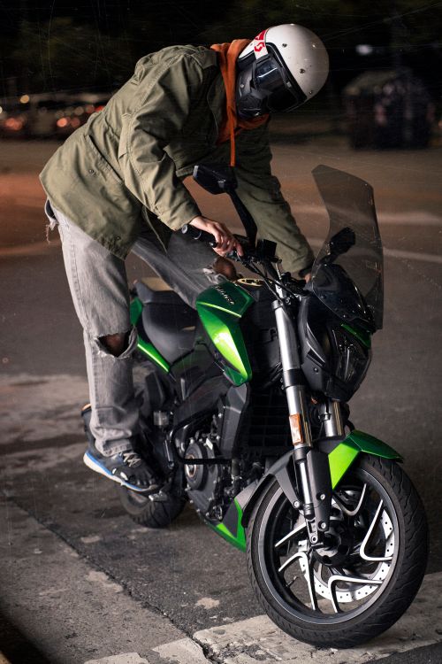 Free Motorcyclist adjusting position on green bike at night street. Stock Photo