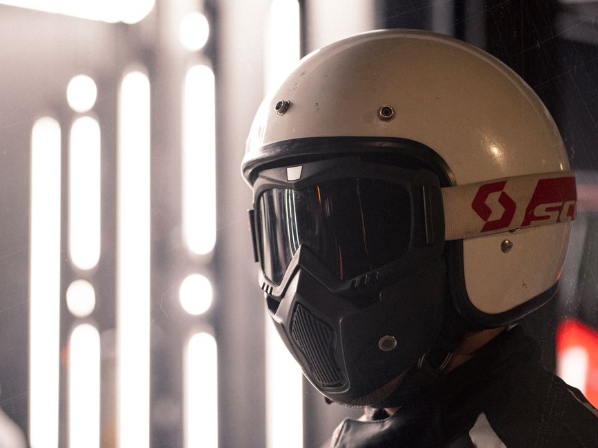 A close-up of a motorcyclist wearing a protective helmet indoors with dramatic lighting.