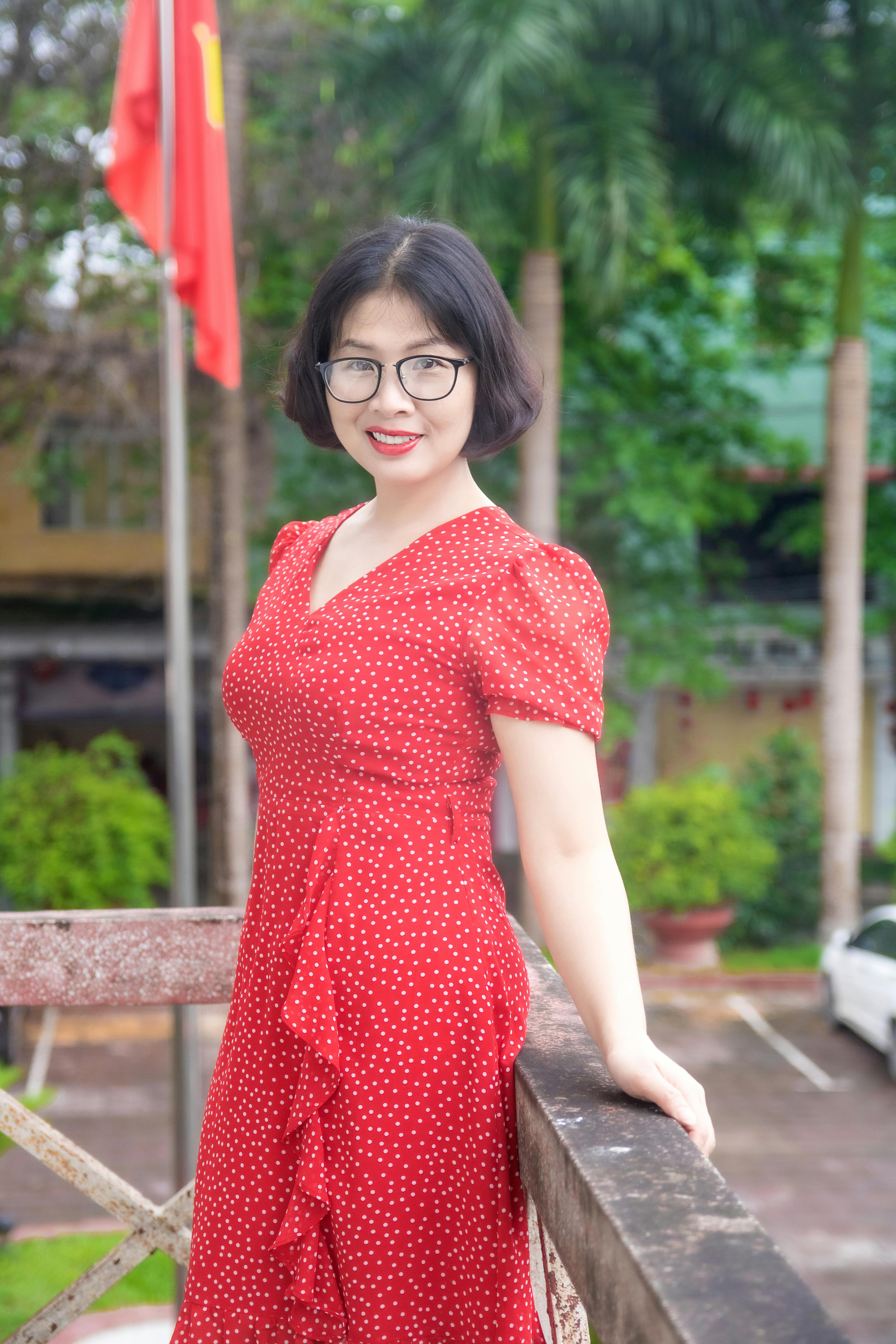 Asian woman with eyeglasses smiling and standing by a railing outdoors in a red dress.