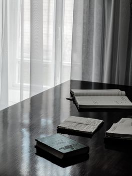 A peaceful reading corner with books on a wooden table by a window with sheer curtains.