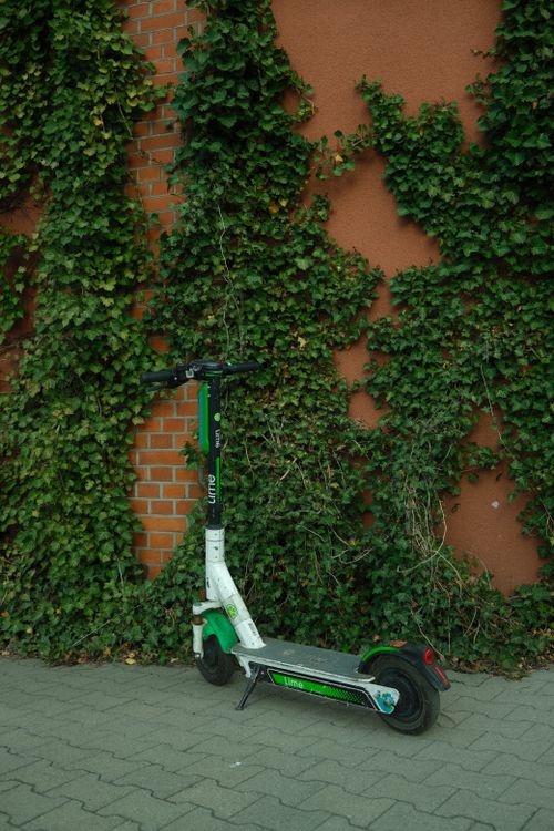Free A parked electric scooter next to a brick wall covered in ivy. Stock Photo