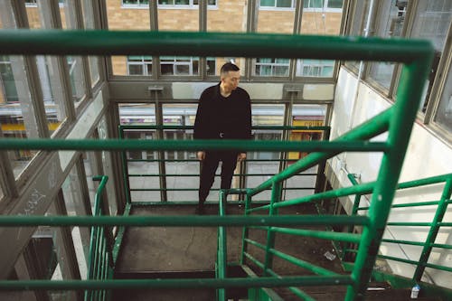 A Man in Black Jacket Standing on Green Metal Stair