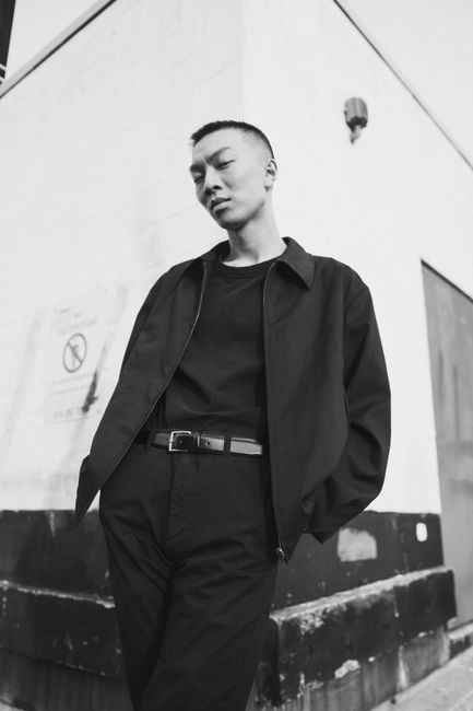 Artistic black and white photo of a man standing against a corner wall.