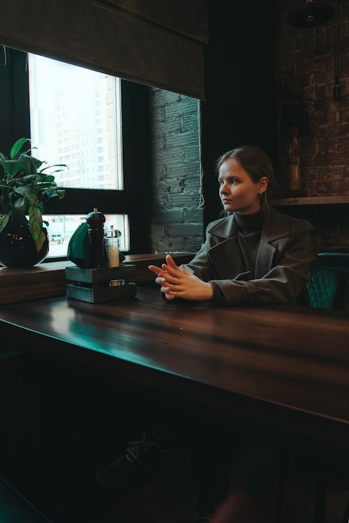 Free A Woman in Gray Coat Sitting Near the Wooden Table Stock Photo