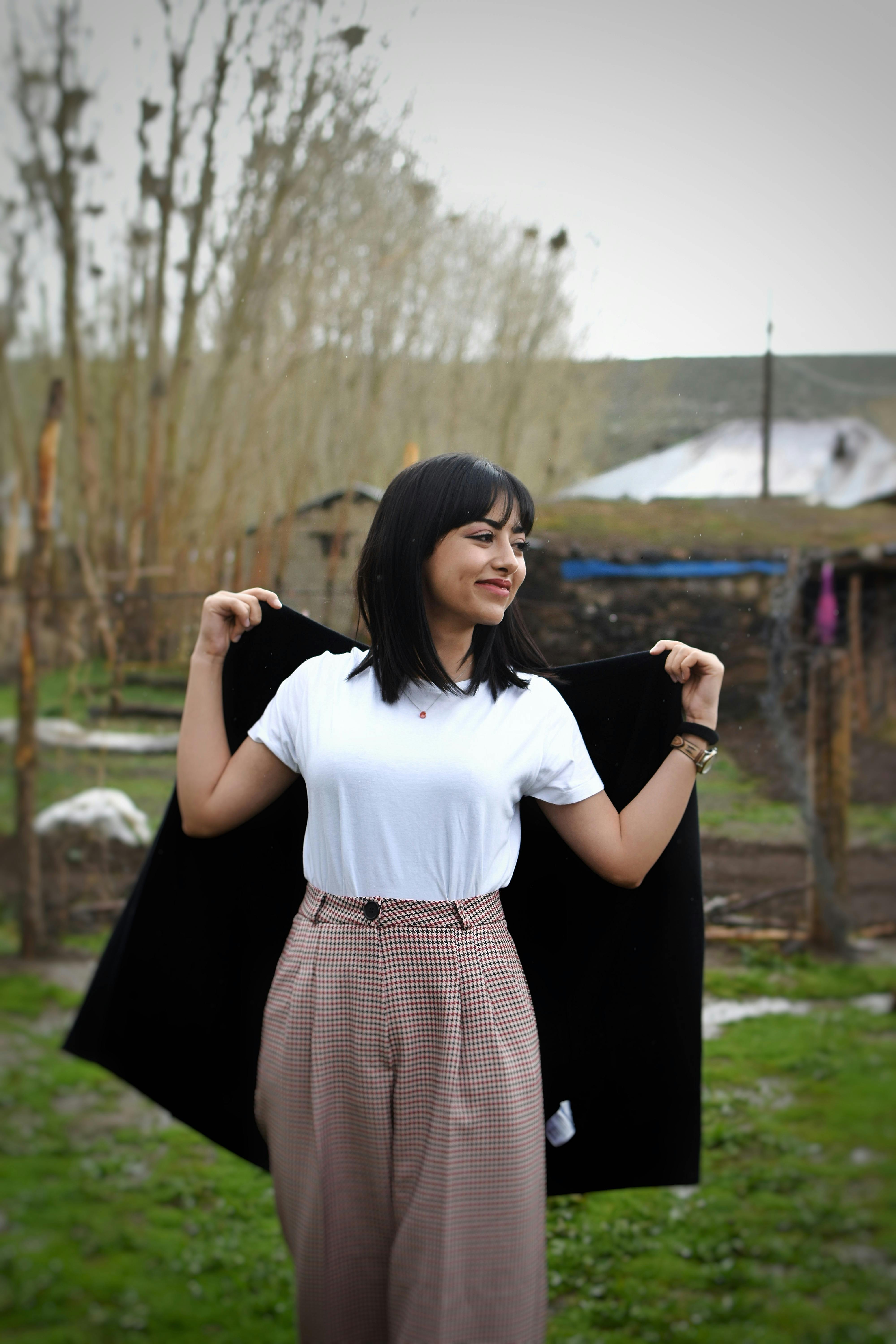 Smiling woman in white shirt and plaid pants posing outdoors holding a black blazer.