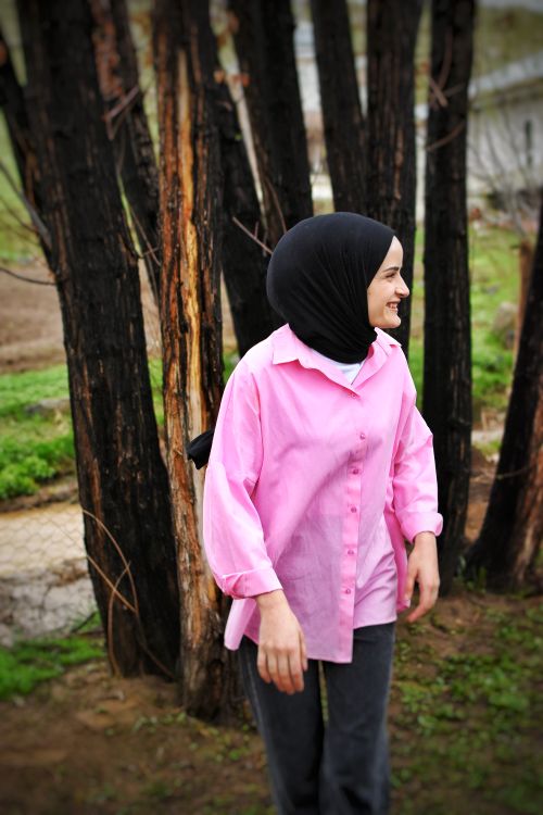 Free A joyful woman in a hijab and pink shirt smiles near trees, captured outdoors. Stock Photo