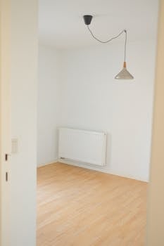 Minimalist empty room with natural light, wooden floors, and modern pendant lamp.