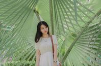 一位年轻女子优雅而宁静地站在热带绿色的棕榈叶中