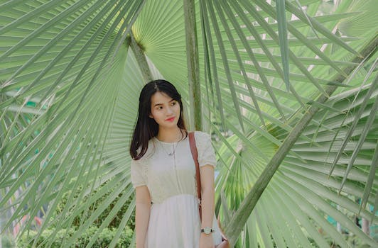 一位年轻女子优雅而宁静地站在热带绿色的棕榈叶中