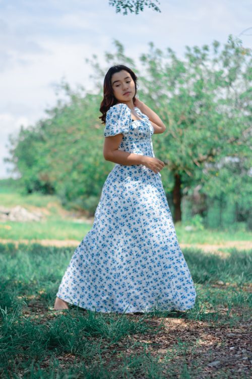 Free A woman in a blue floral dress poses barefoot on grass, under sunny skies. Stock Photo