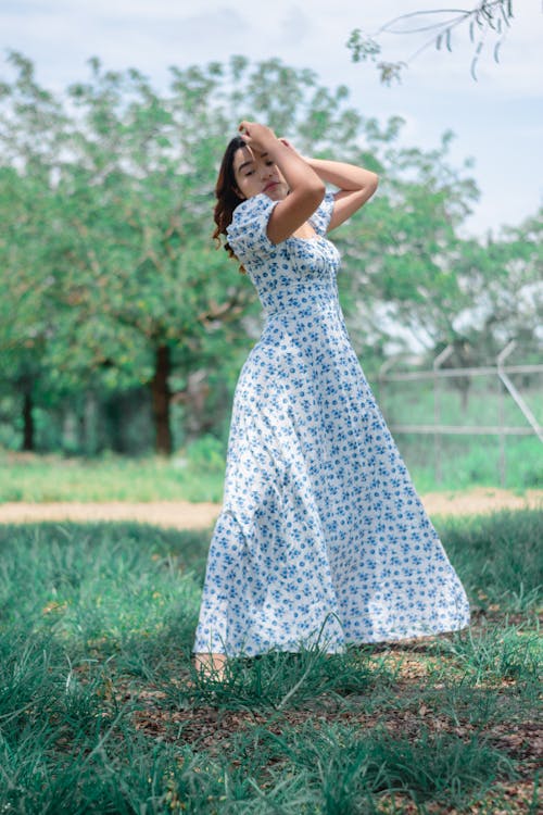 Woman in White and Blue Floral Dress Standing on Green Grass Field
