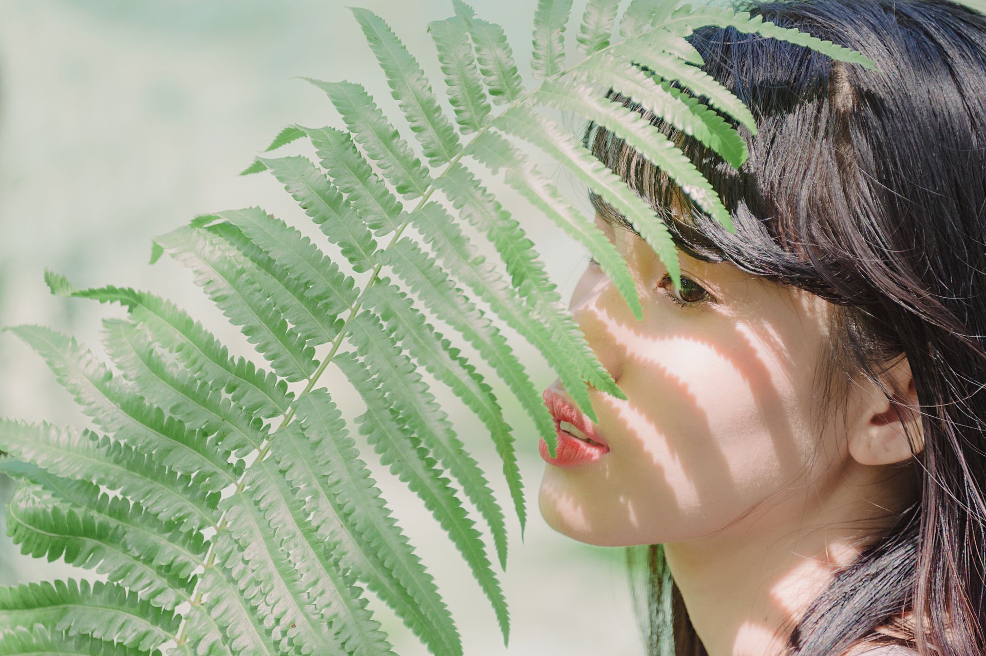 Beautiful portrait of a young woman with fern leaves casting shadows on her face.