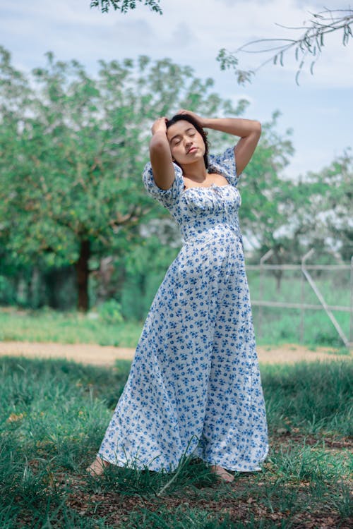 Woman in White and Blue Floral Dress Standing on Green Grass Field
