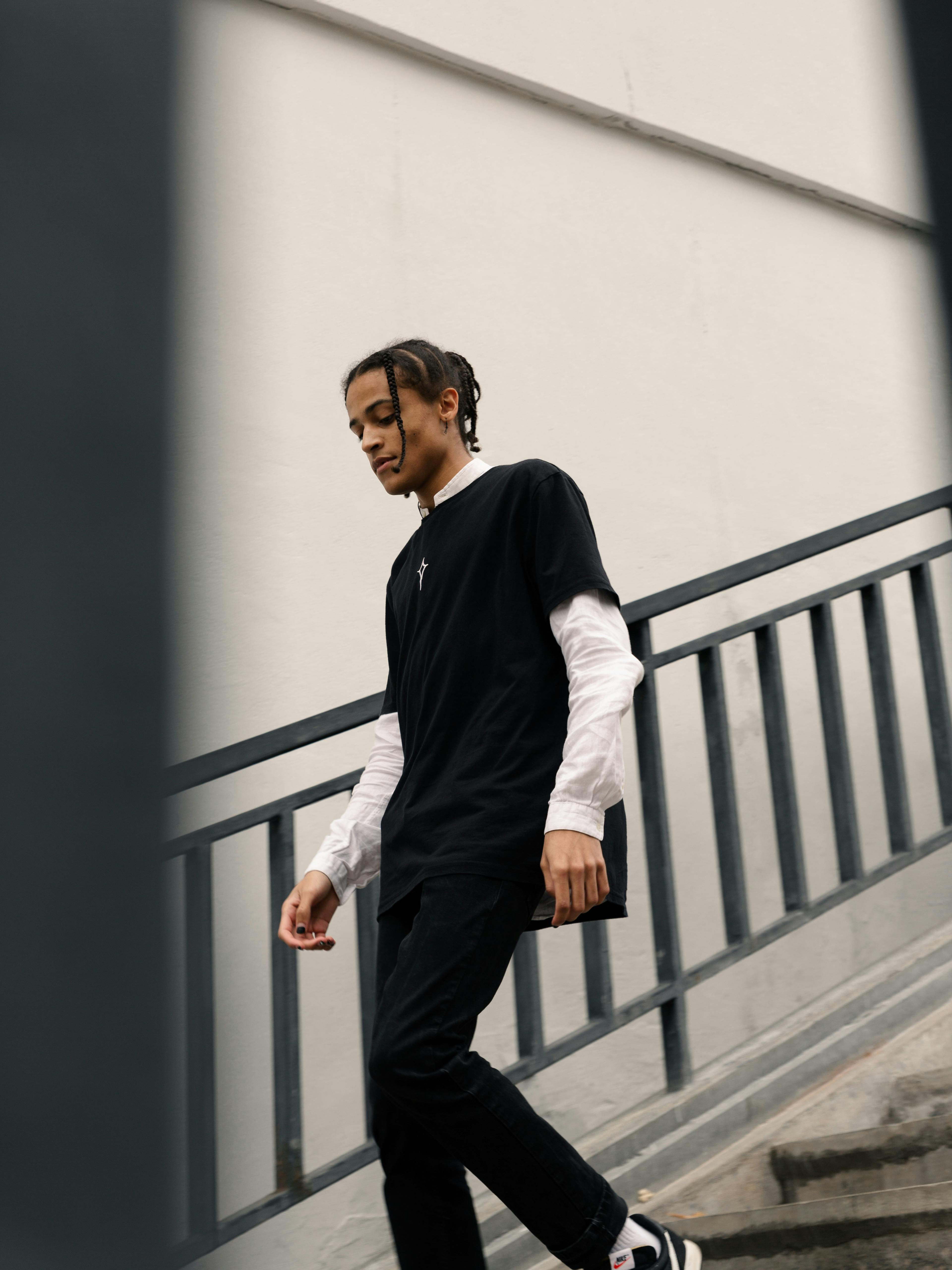Profile view of a young man walking down an outdoor urban staircase in a casual outfit.