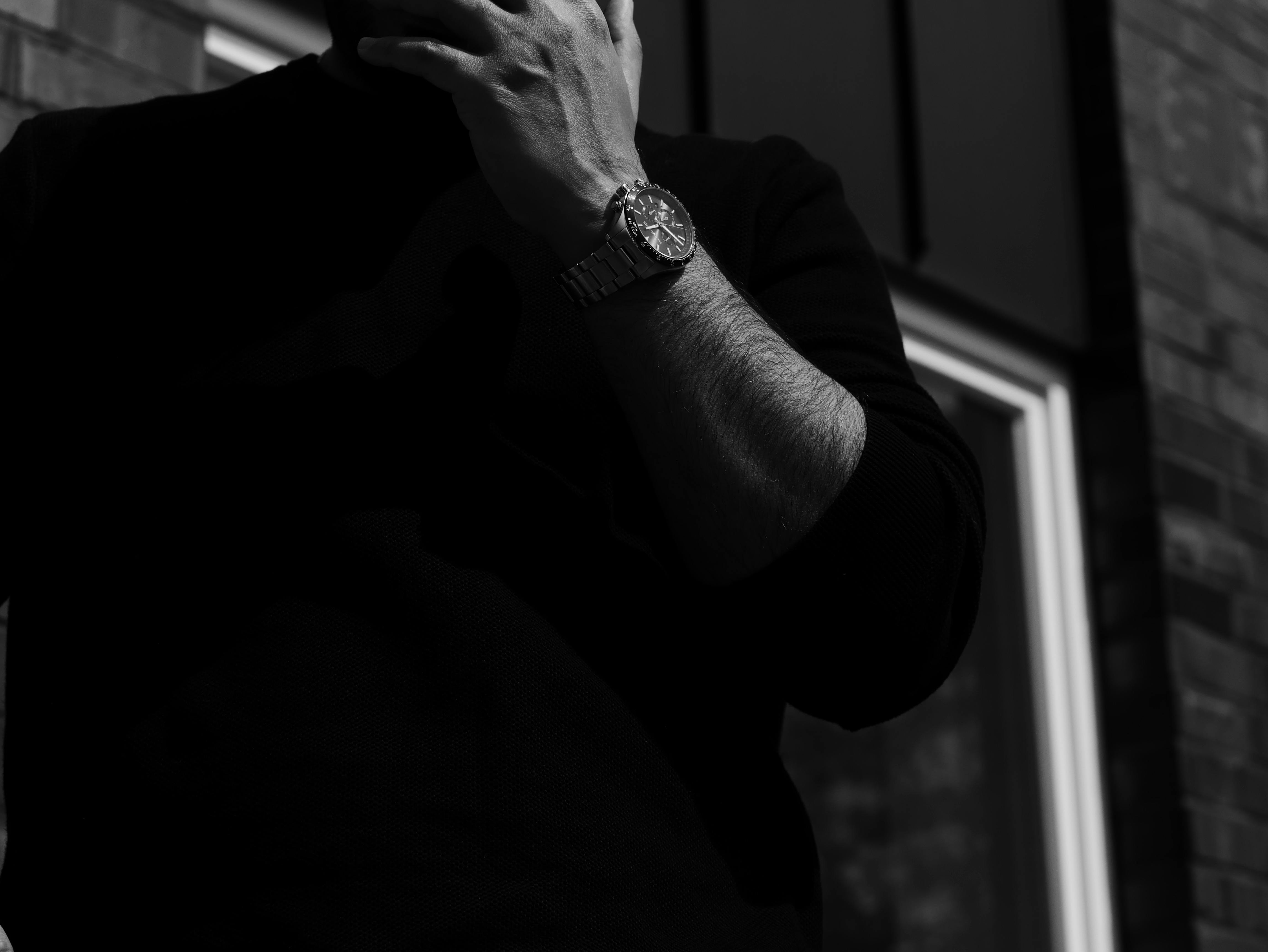 Dramatic black and white image of a man with a wristwatch in shadow.