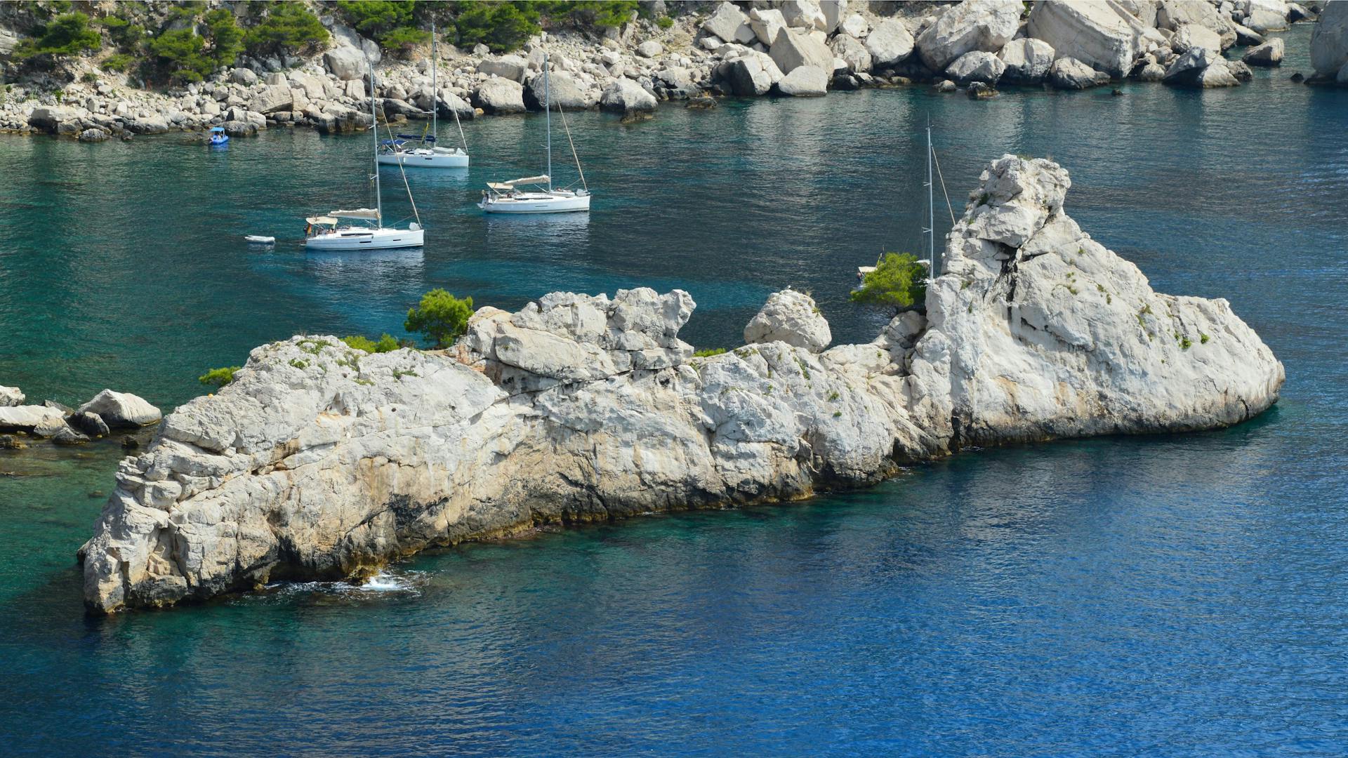 Yachts anchored by a rocky coastline with crystal clear blue water.