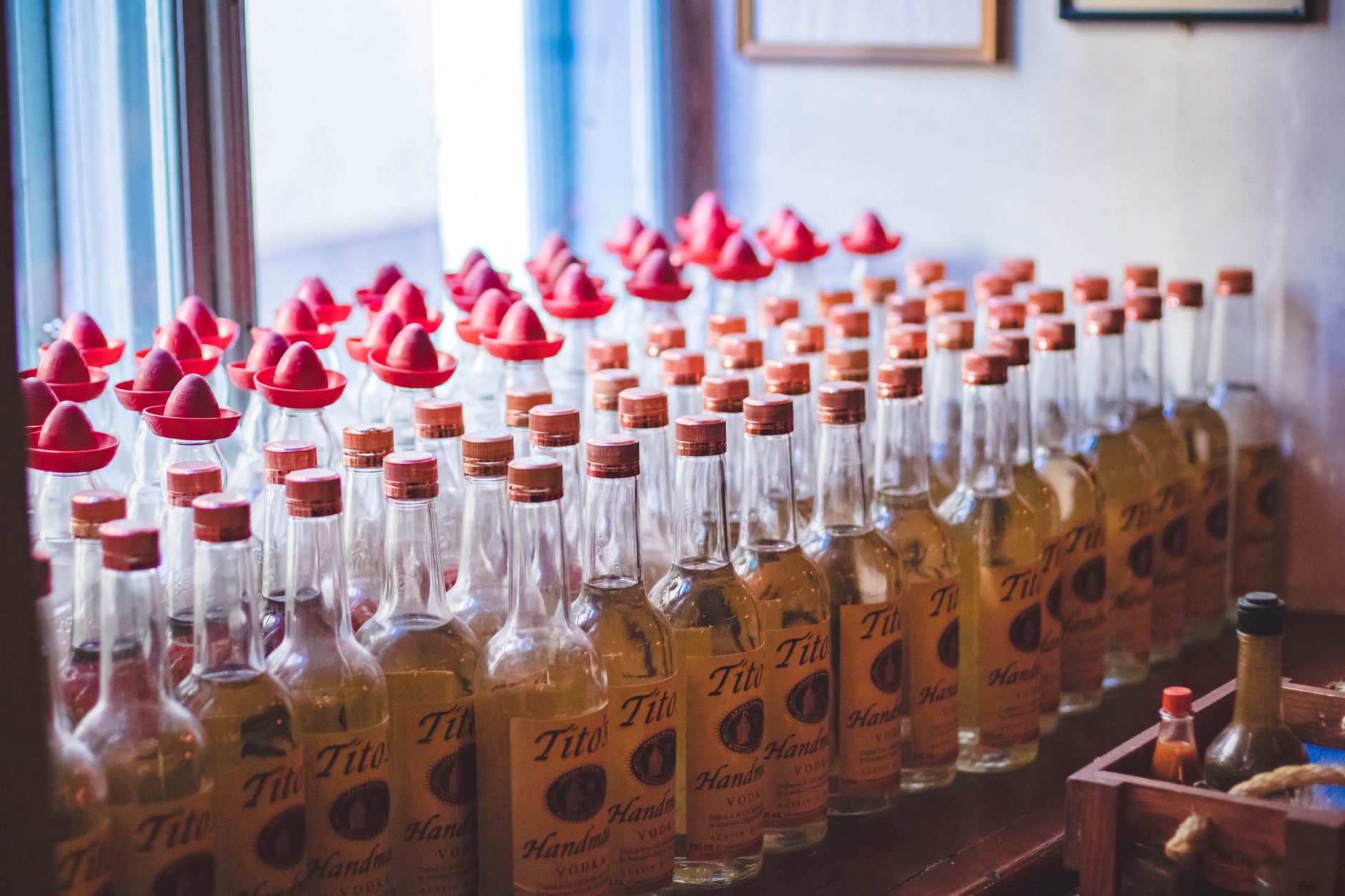 Bottles displayed with red sombrero caps on a wooden shelf in a cozy indoor setting.