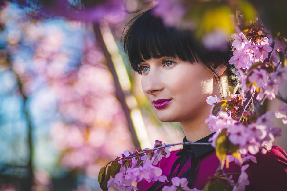 Close-up portrait of a woman surrounded by cherry blossoms showcasing spring beauty and fashion.