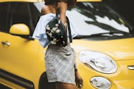 一位穿着时尚的女人站在一辆黄色汽车旁，展示着她的服装和包