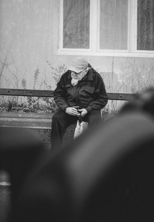 Free Grayscale Photo of Woman in Black Coat and Black Pants Sitting on Bench Stock Photo
