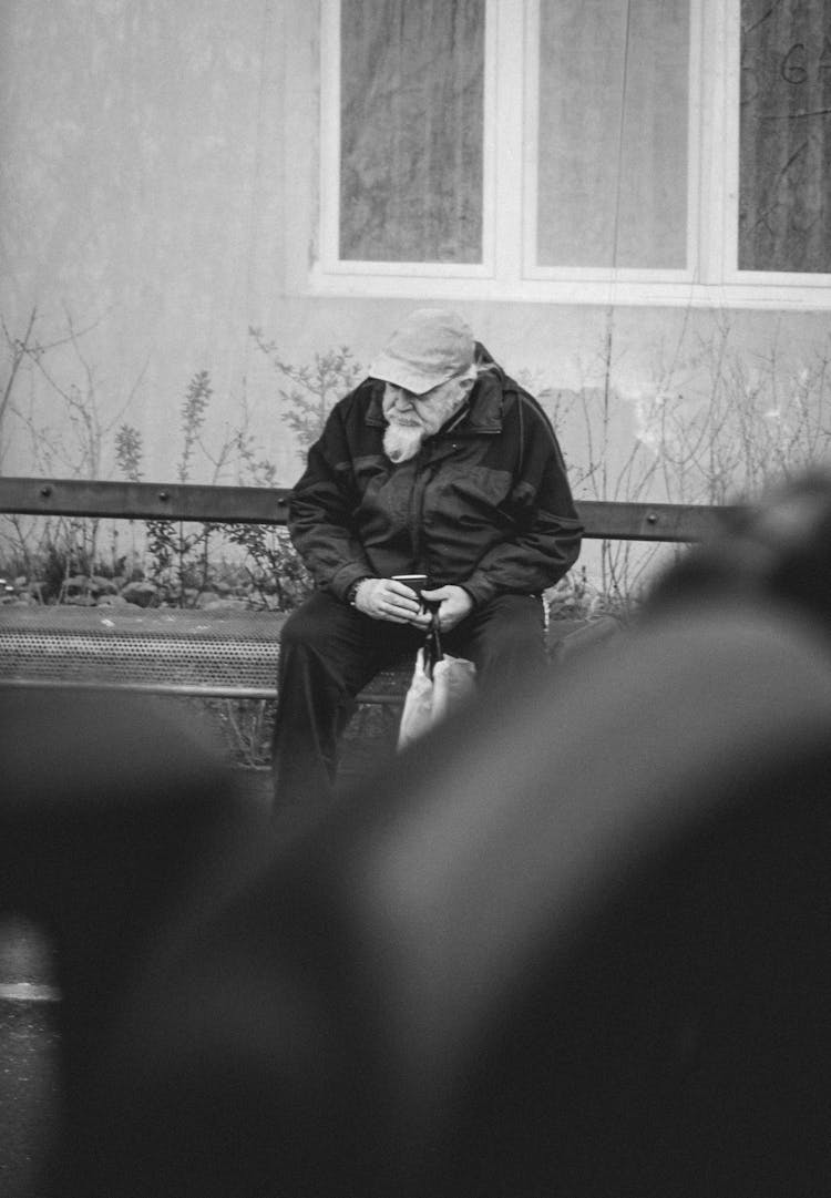 Grayscale Photo Of Man In Black Jacket Sitting On Bench