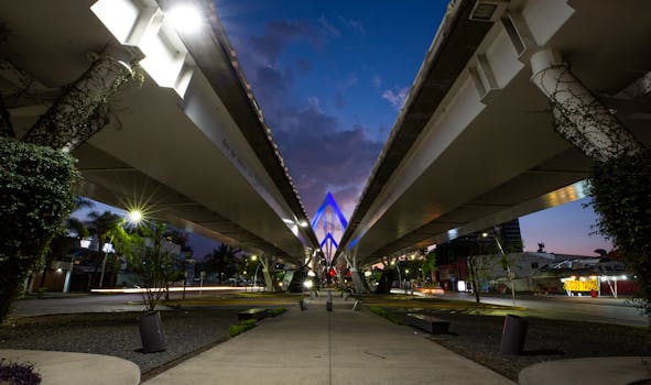 A night shot of the illuminated Matute Remus Bridge in Guadalajara with a vibrant sunset background.