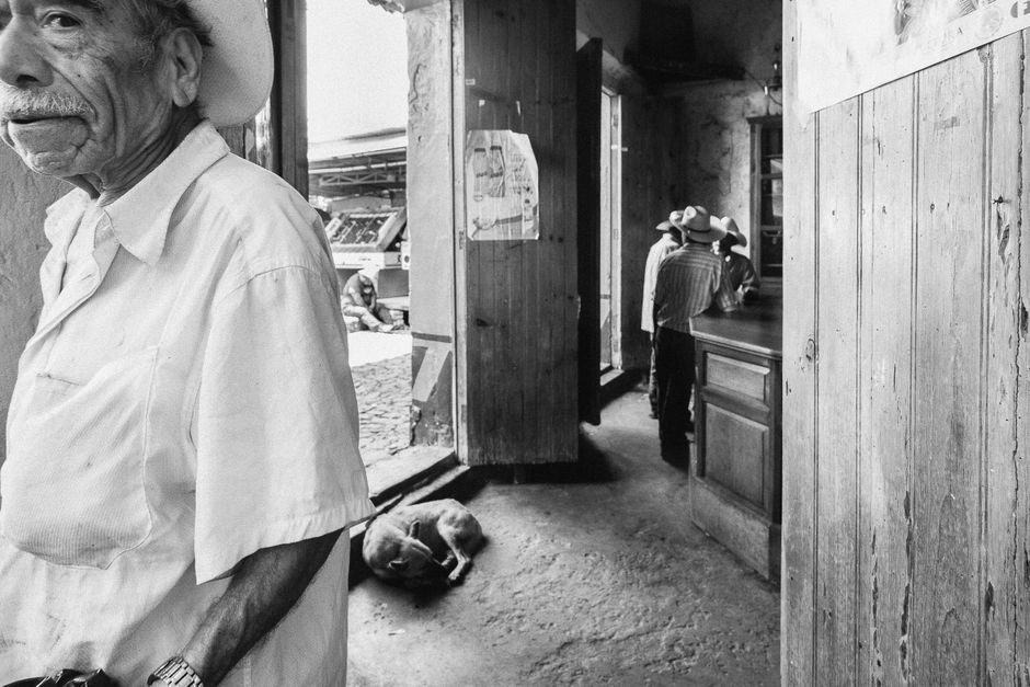 Atmospheric black and white scene in a Mexican canteen with people and a dog.