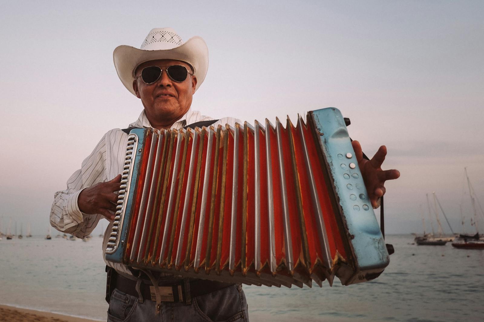Uomo con cappello da cowboy suona fisarmonica vicino al mare