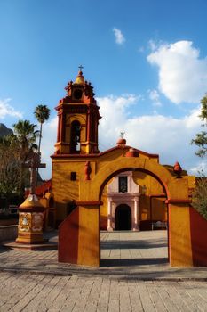 A vibrant colonial church with striking colors and clear blue sky in a Mexican town square.