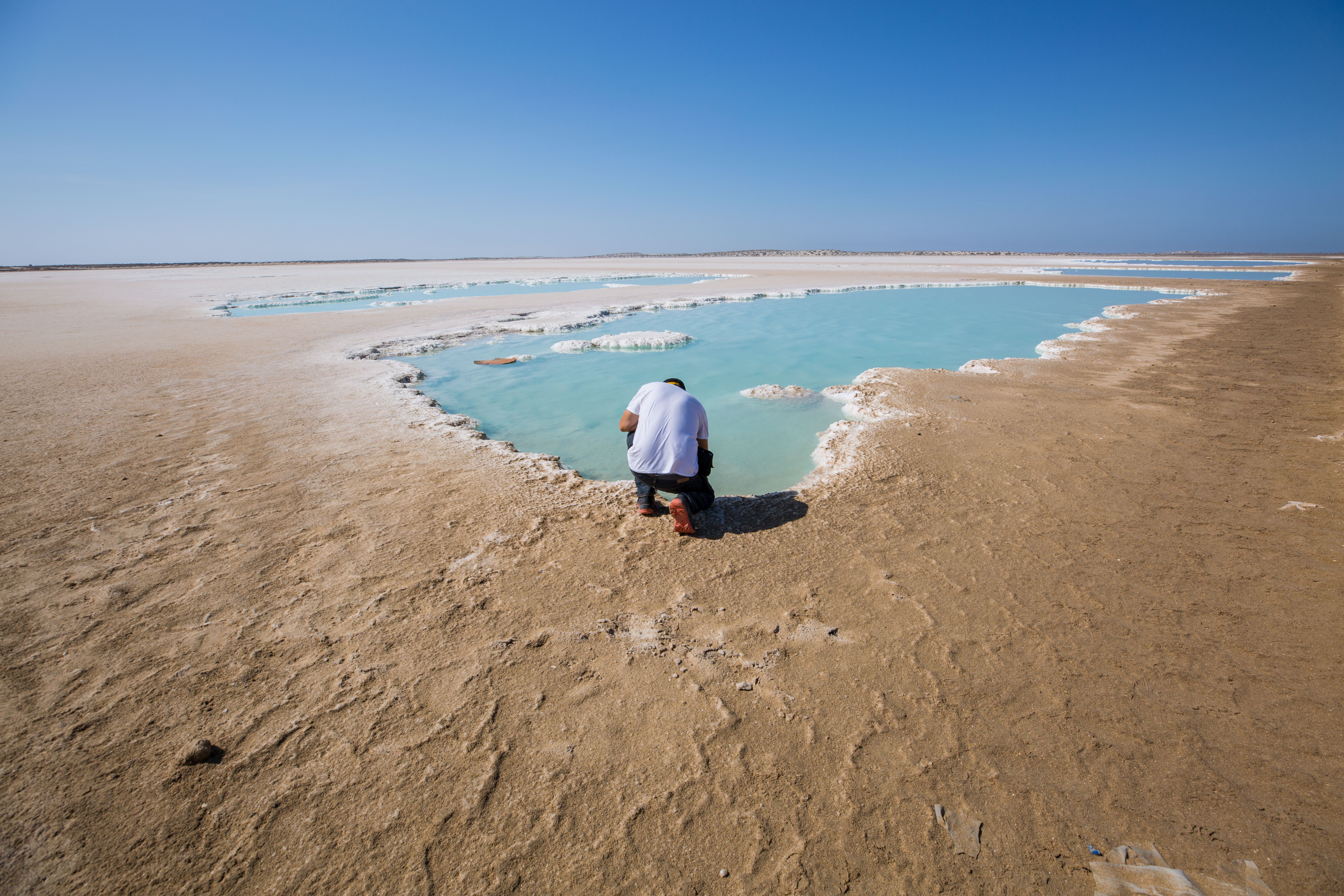 A man kneels by a turquoise water pool in Guerrero Negro's salt flats, Mexico.