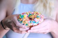 一个人正在展示一个有趣又充满活力的甜点，上面有美味的甜甜圈和五颜六色的谷物浇头