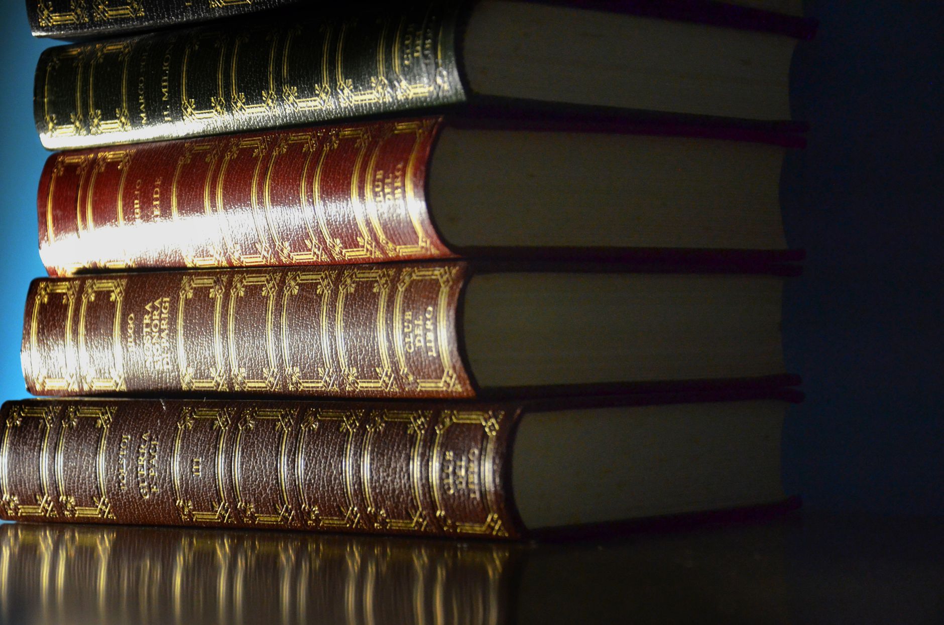 A stack of vintage leather-bound books with decorative spines reflecting light.