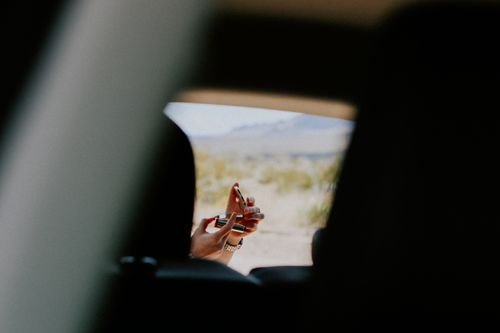 Free A woman applying red lipstick using a compact mirror outside a vehicle in a desert setting. Stock Photo