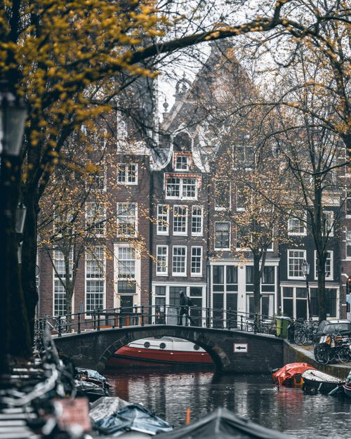Free A scenic view of an Amsterdam canal, picturesque bridge, and historic buildings in fall. Stock Photo