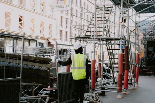 A construction worker onsite in a city wearing safety gear and examining scaffolding.
