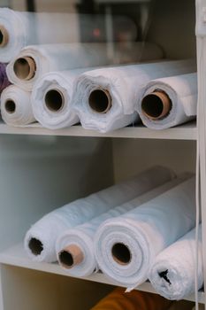 White rolls of fabric stacked on shelves, ideal for textile and fashion projects.